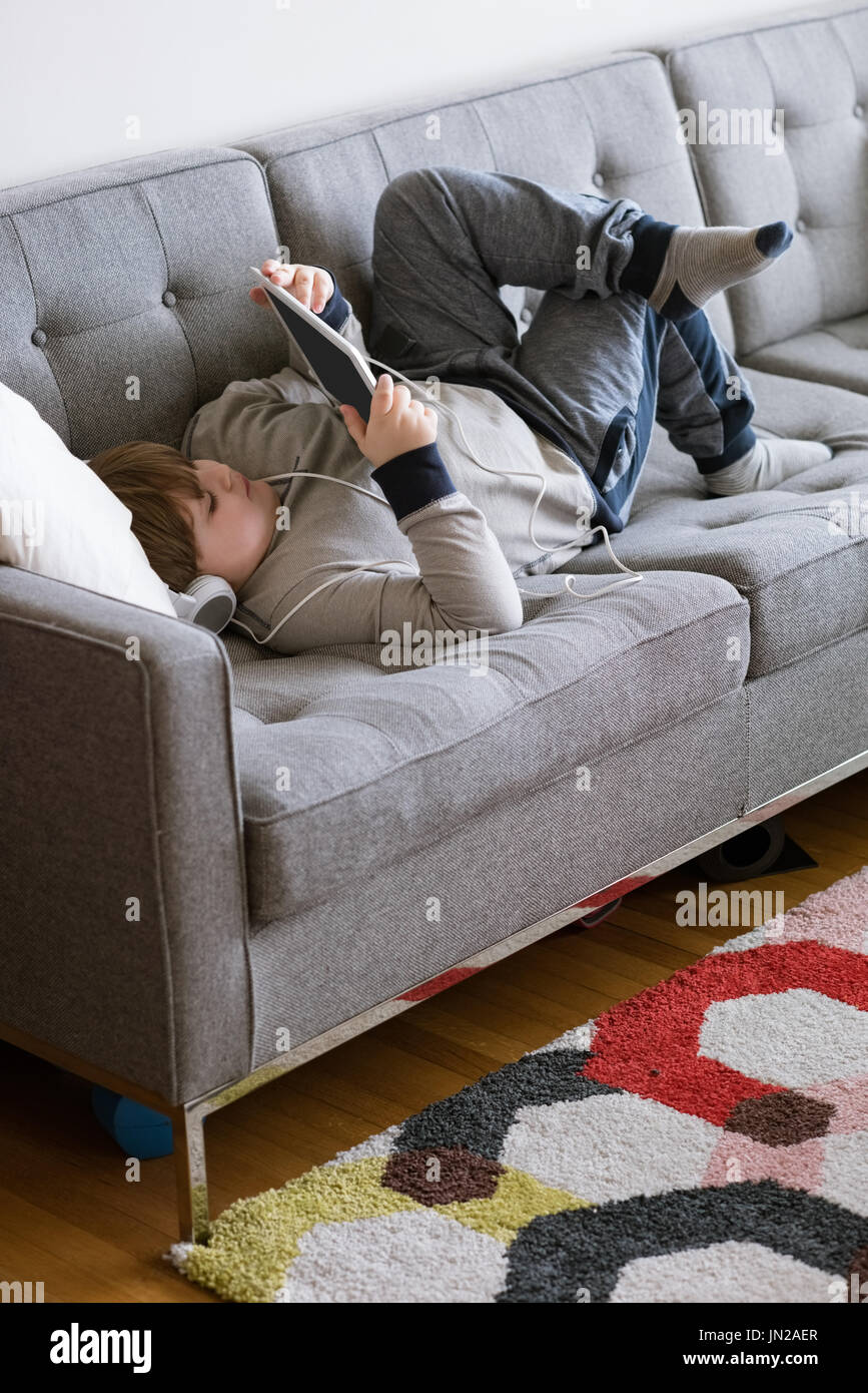Full length of boy using digital tablet while lying on sofa Stock Photo