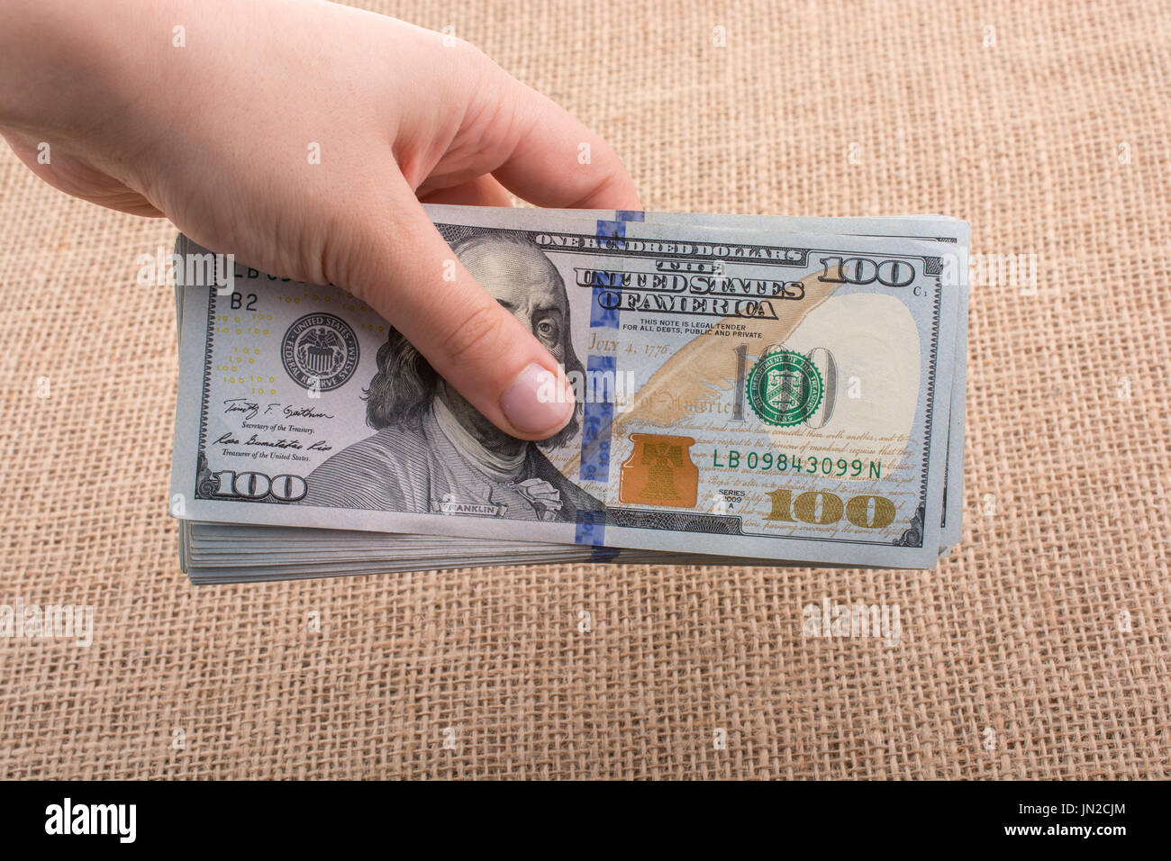Hand holding banknote bundle of US dollar on a linen canvas background ...