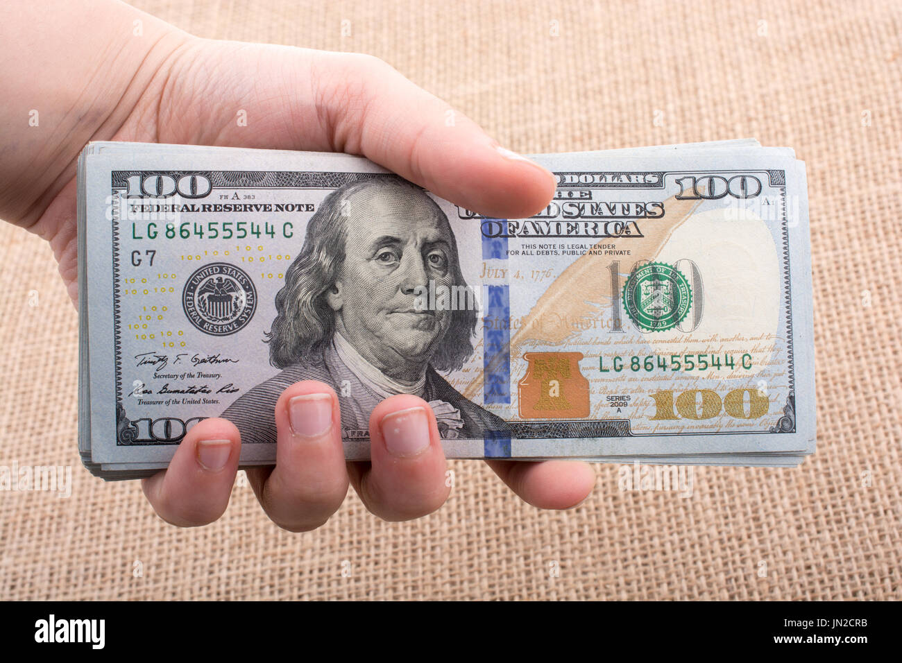 Hand holding banknote bundle of US dollar on a linen canvas background ...