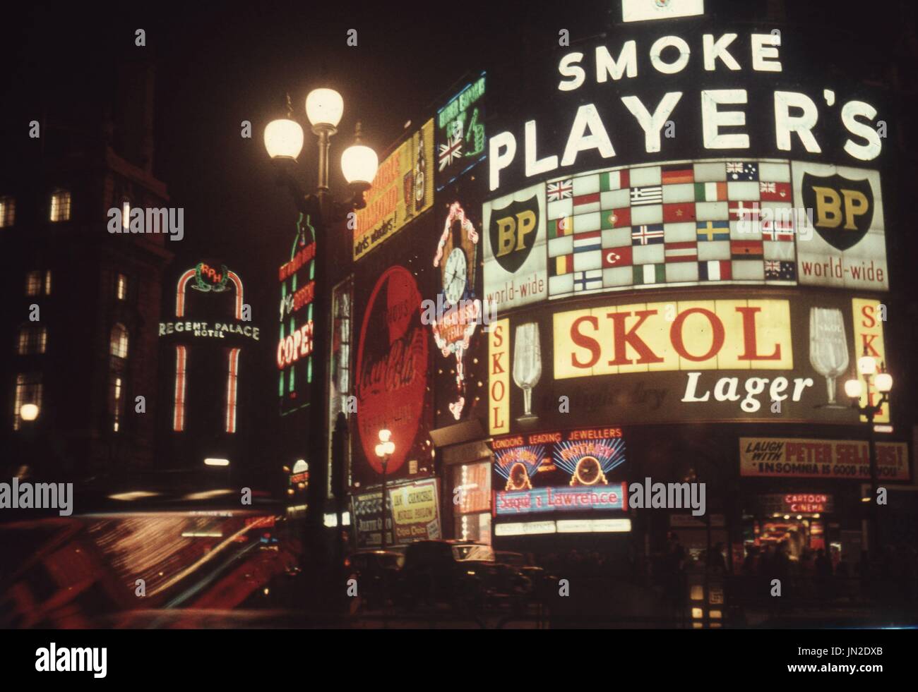 Piccadilly Circus, London, England 1957. The bright night lights of Piccadilly Circus in London, England in 1957. Dominated by a Players Cigarette advert and dated by the advert for the Insomnia Is Good For You movie, an early appearance of Peter Sellars before he became famous (see bottom right of picture).   Photograph by Tony Henshaw Stock Photo