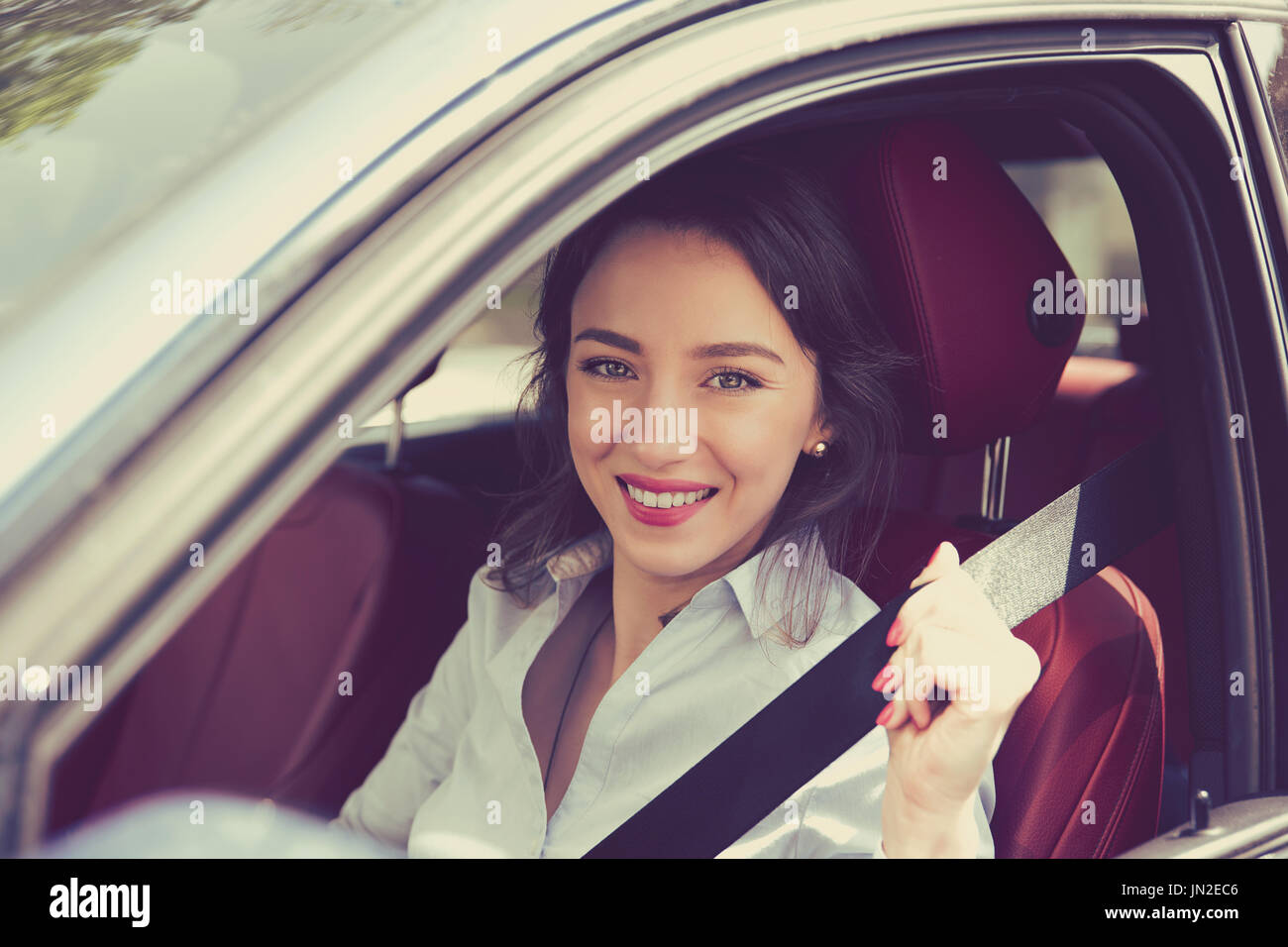 Young woman pulling on seat belt inside her new car. Life saving