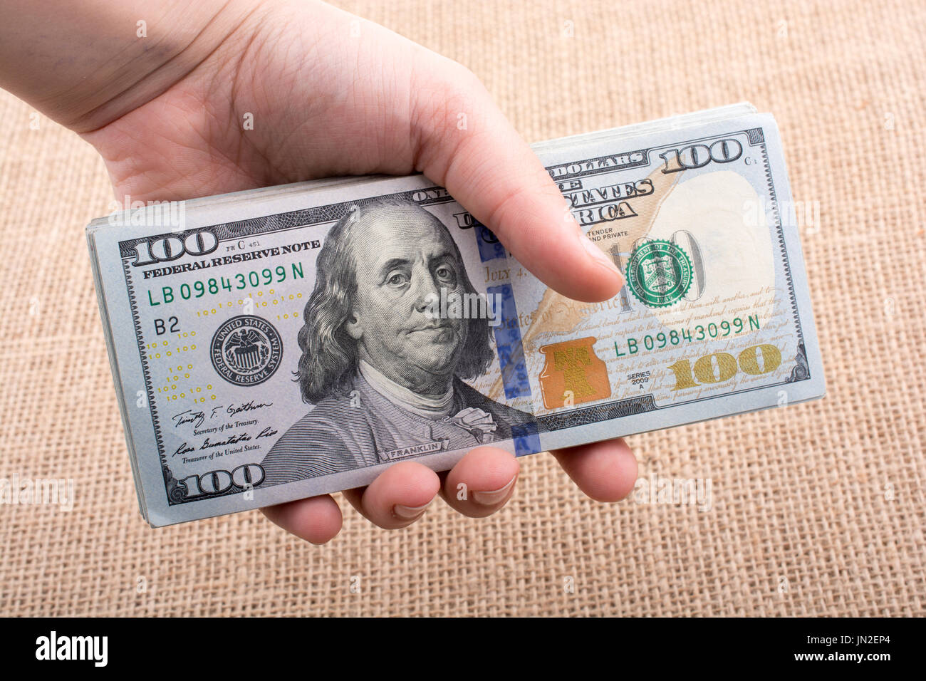 Hand holding banknote bundle of US dollar on a linen canvas background ...