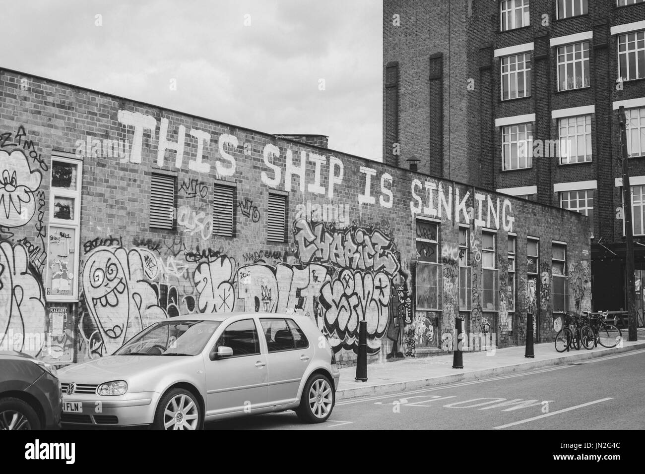 Street in Hackney Wick, east London, with graffiti on wall reading 'This ship is sinking'. Stock Photo