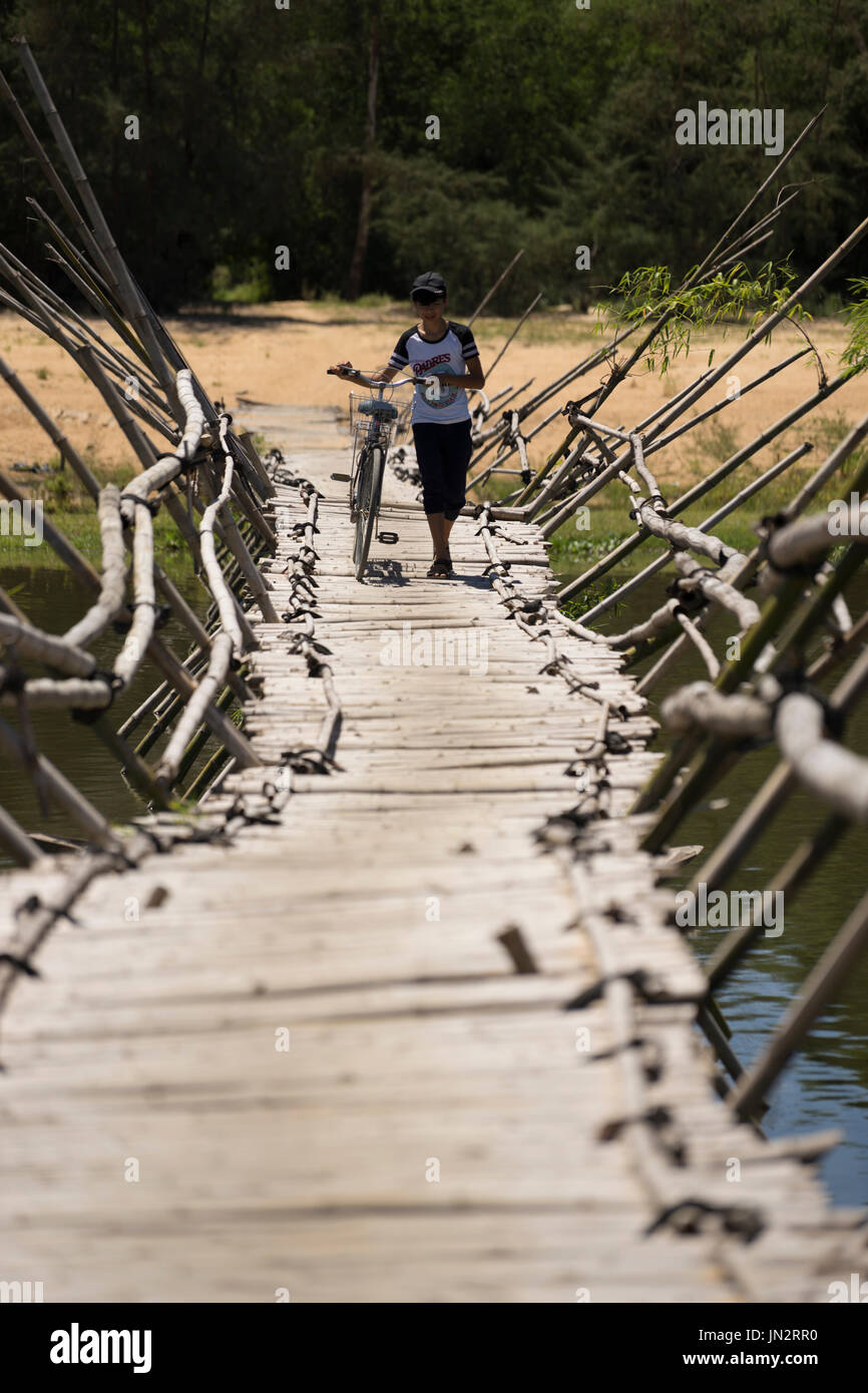 Vietnamese boy walking his bicycle across a traditional bamboo bridge in rural Vietnam Stock Photo