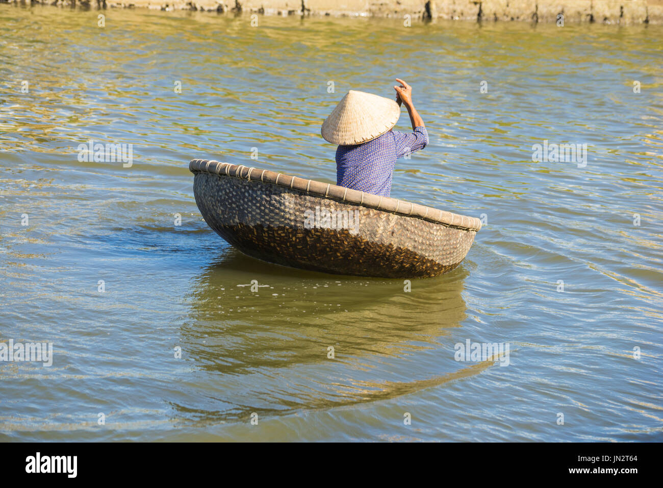 Vietnamese woman padding traditional round woven bamboo boat across river Stock Photo