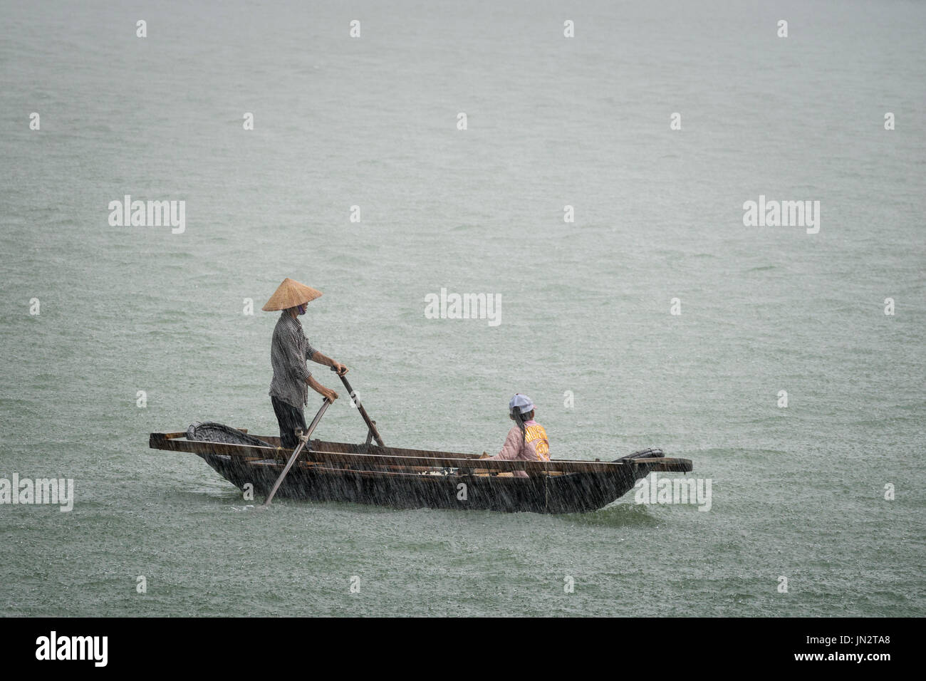 Vietnamese father and daughter in a row boat caught in the pouring rain during a storm at sea Stock Photo