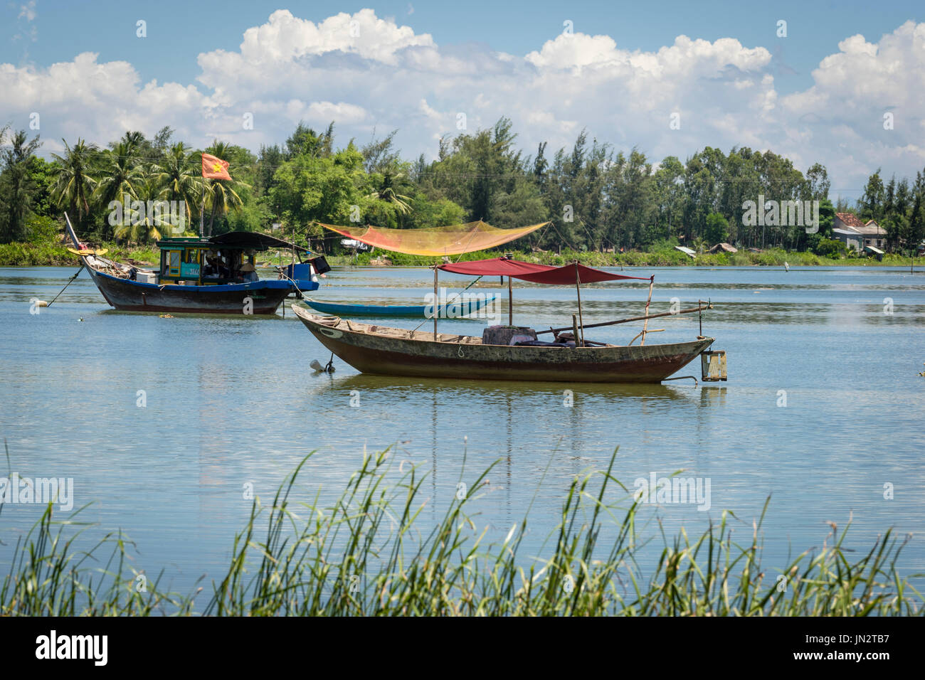 Old fashioned Vietnamese fishing boat and row boat moored on Thu Bon River outside Hoi An Vietnam Stock Photo
