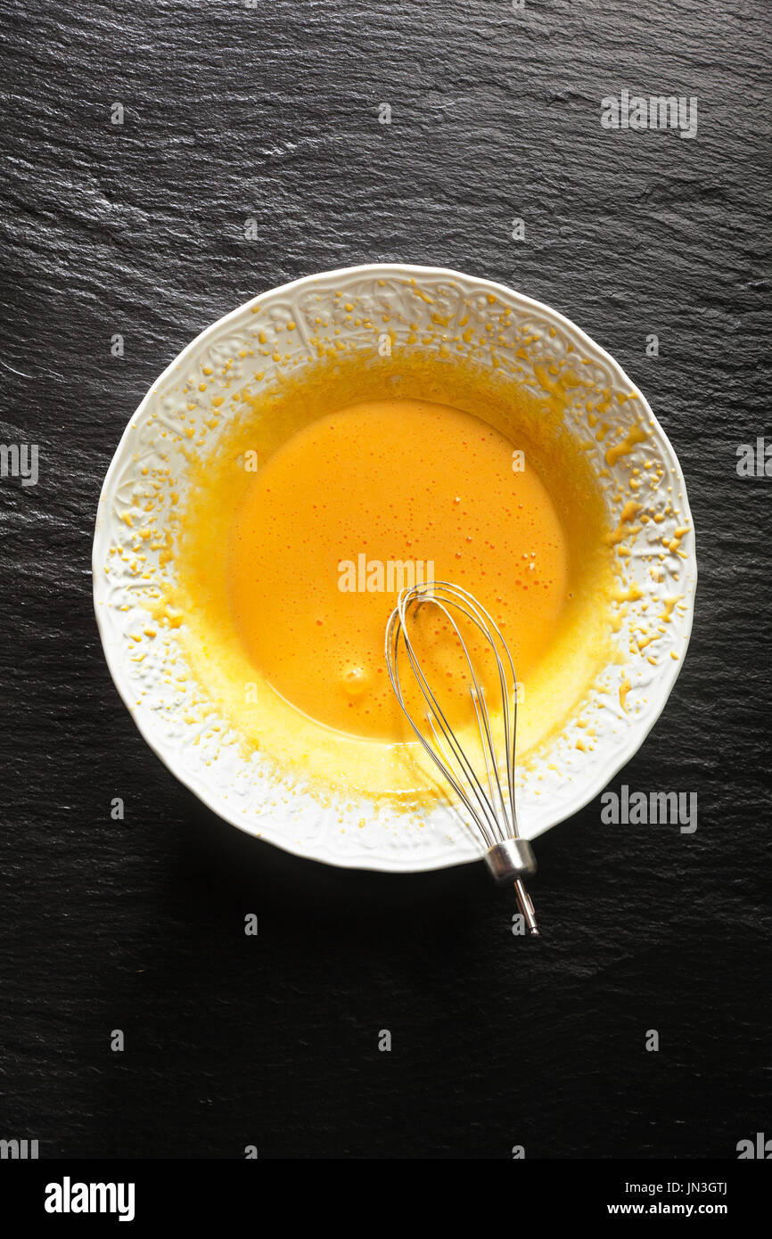 Whipped egg yolks in a white bowl and a top from an electric mixer with a black stone table