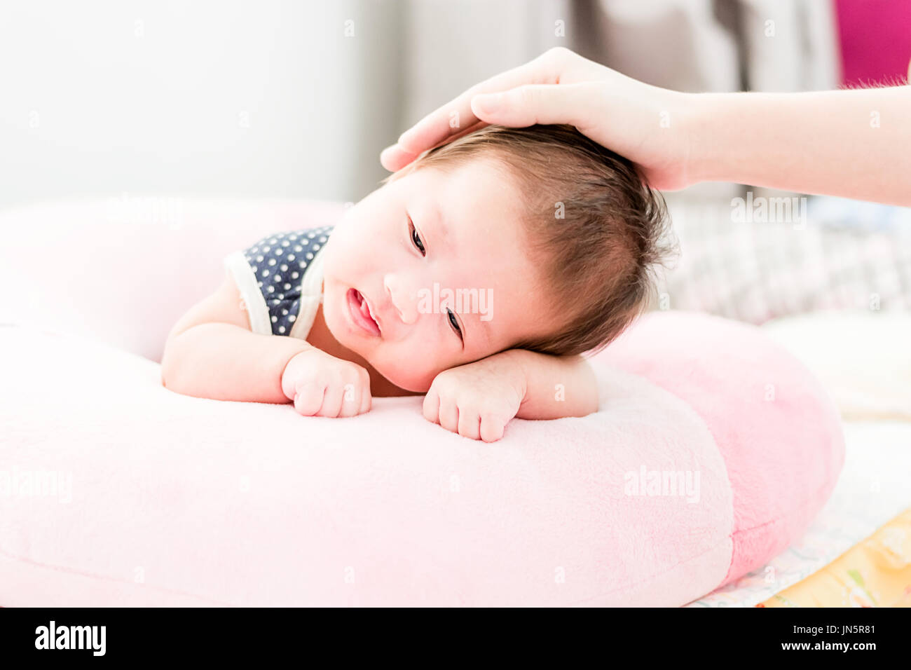 Portrait of a little adorable infant baby girl lying on the tummy on the pillow with mother hand stroking her head Stock Photo