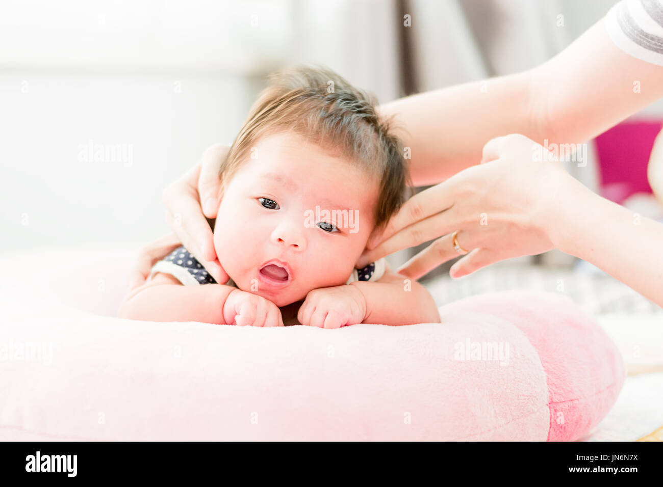 Portrait of a little adorable infant baby girl lying on the tummy on the pillow with mother hand stroking her head Stock Photo