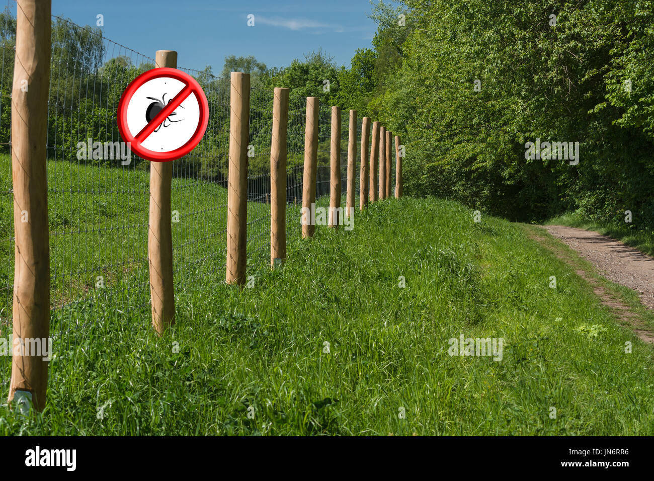 Red shield with crossed out ticks symbol on a fence post in front of a green meadow. Concept Ticks free zone Stock Photo
