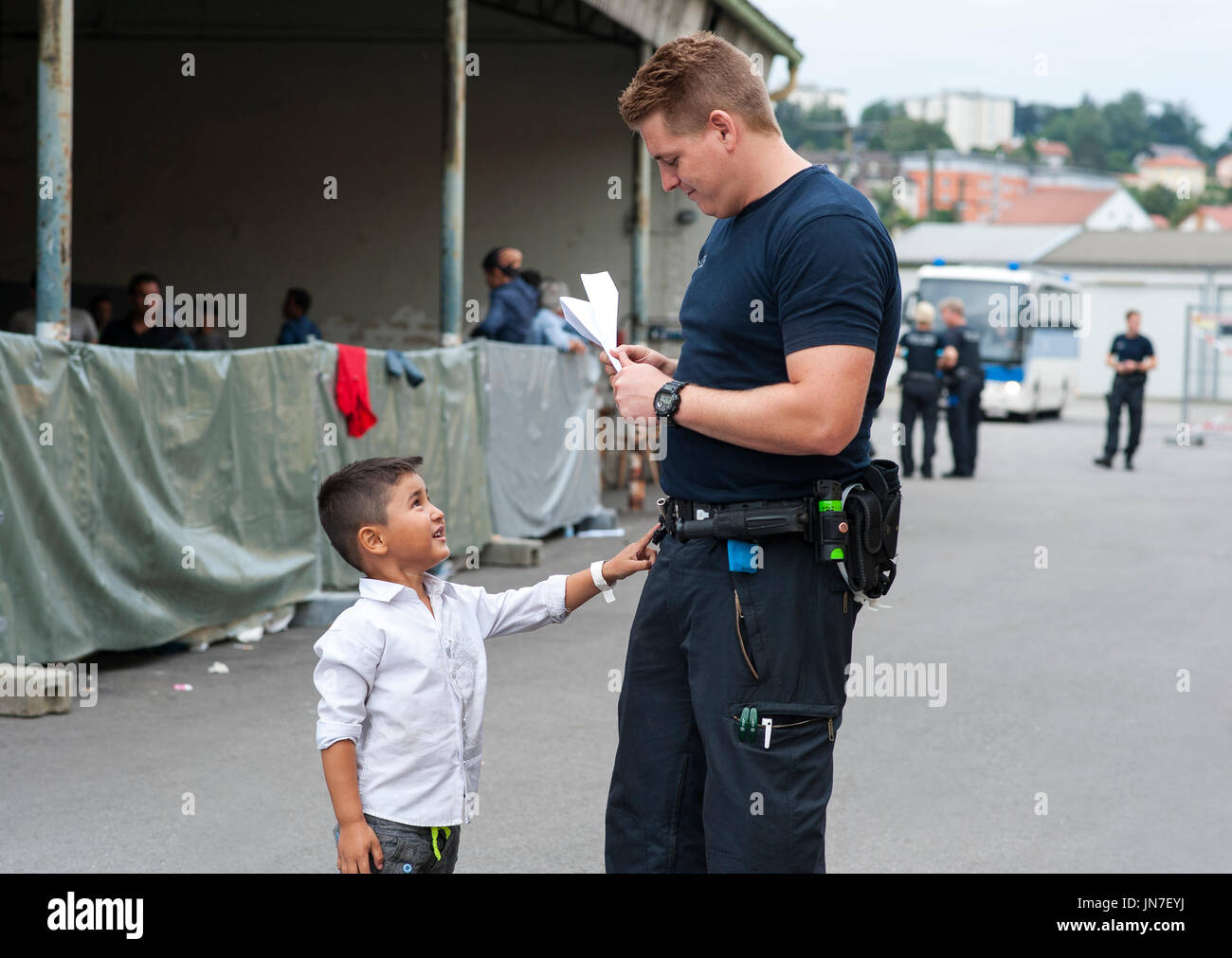 Police officer with a young Syrian refugee boy at the registration center in Passau, Germany. The officer talks to the little boy. Stock Photo