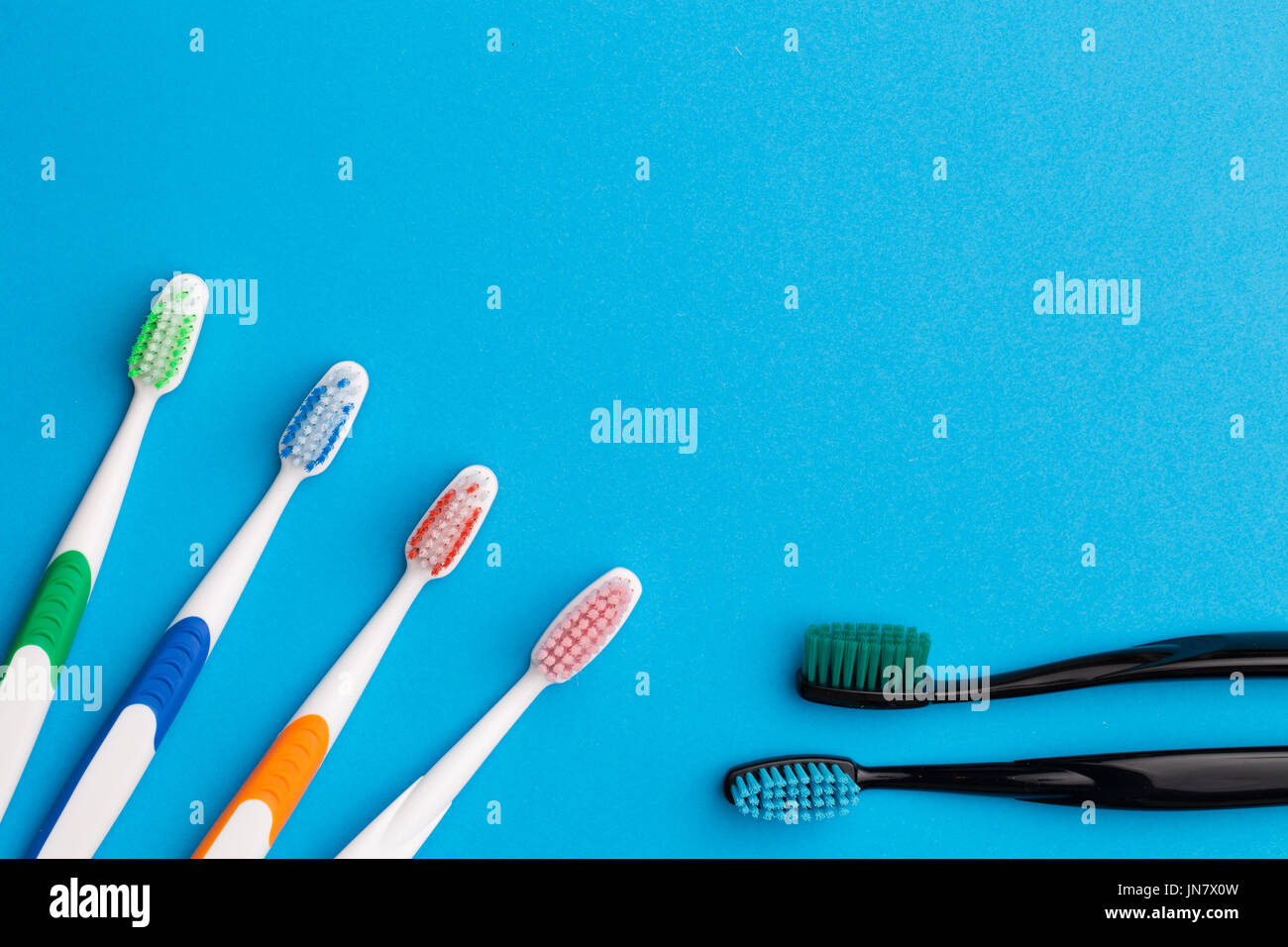 Four multicolored and two black toothbrushes on empty blue background, place for words Stock Photo