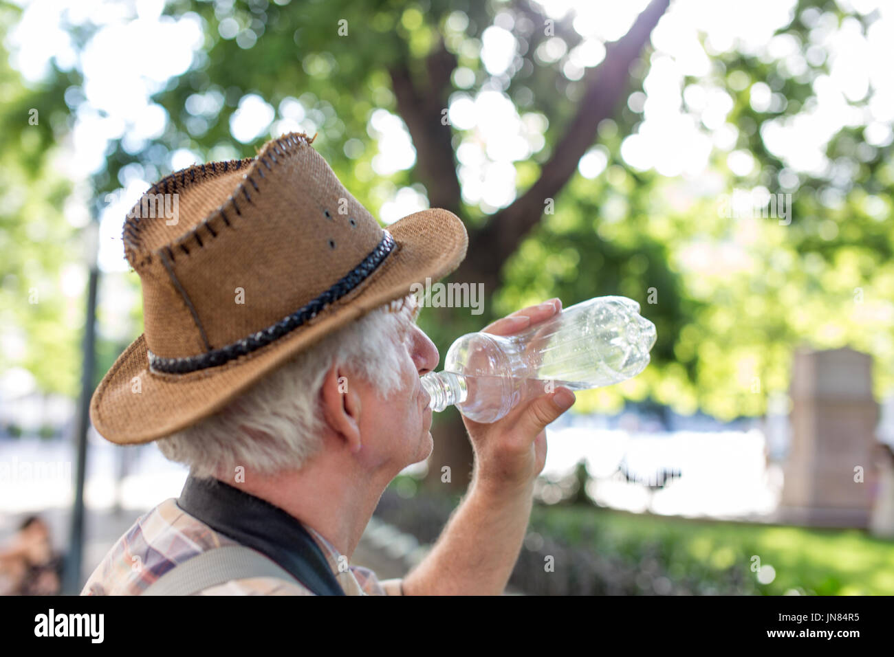 Senior thirsty tourist man drinking water from bottle in park Stock Photo