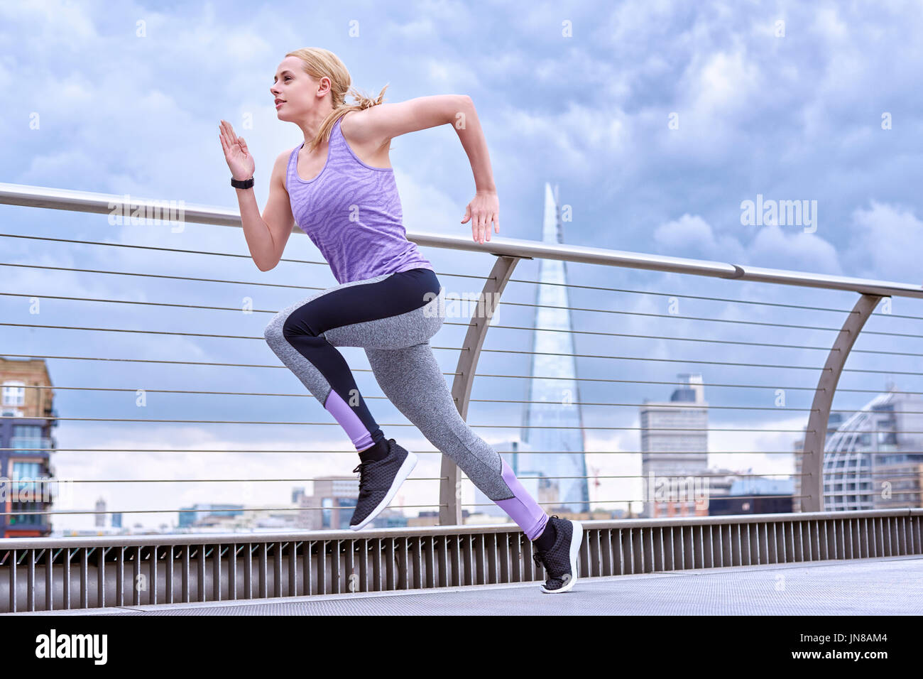 A young woman sprints along the Millennium Footbridge with The Shard in the background Stock Photo