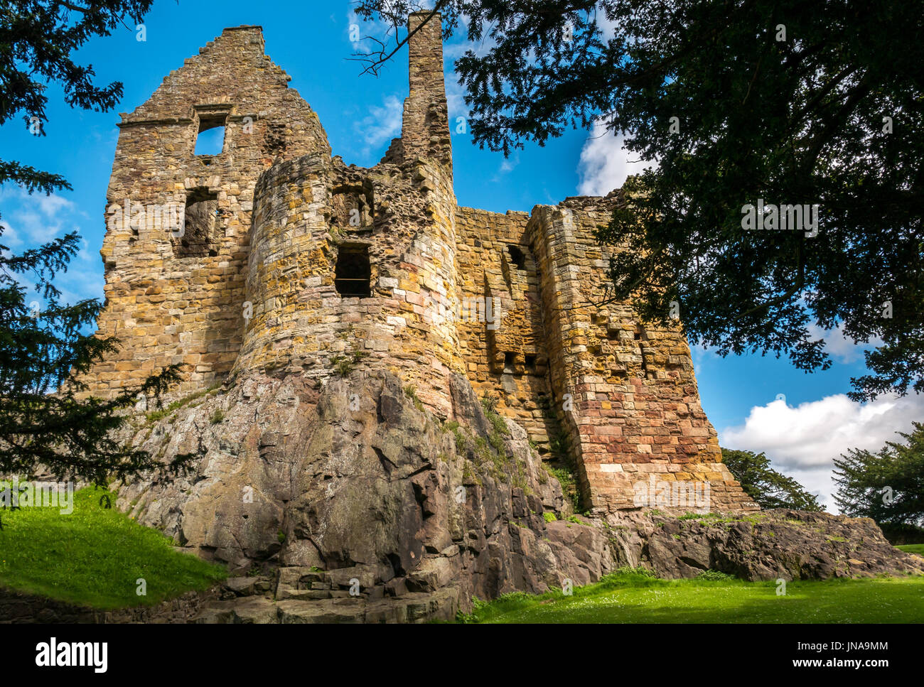 Tree framed view of high sunlit ruined stone walls of 13th century medieval Dirleton Castle, East Lothian, Scotland, UK, with blue sky Stock Photo