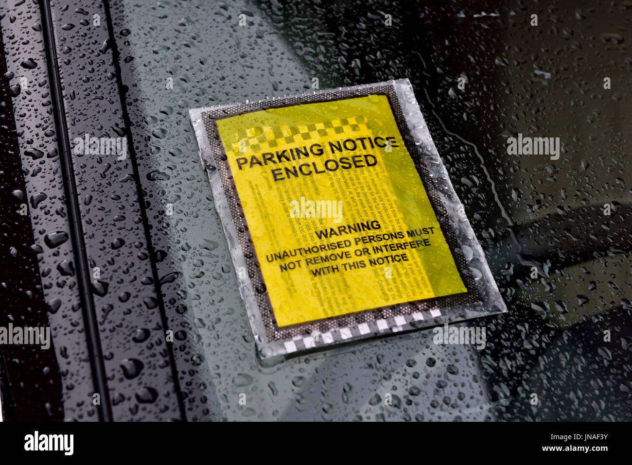 Ticket 'Parking Notice Enclosed' on car windscreen in the rain Stock Photo
