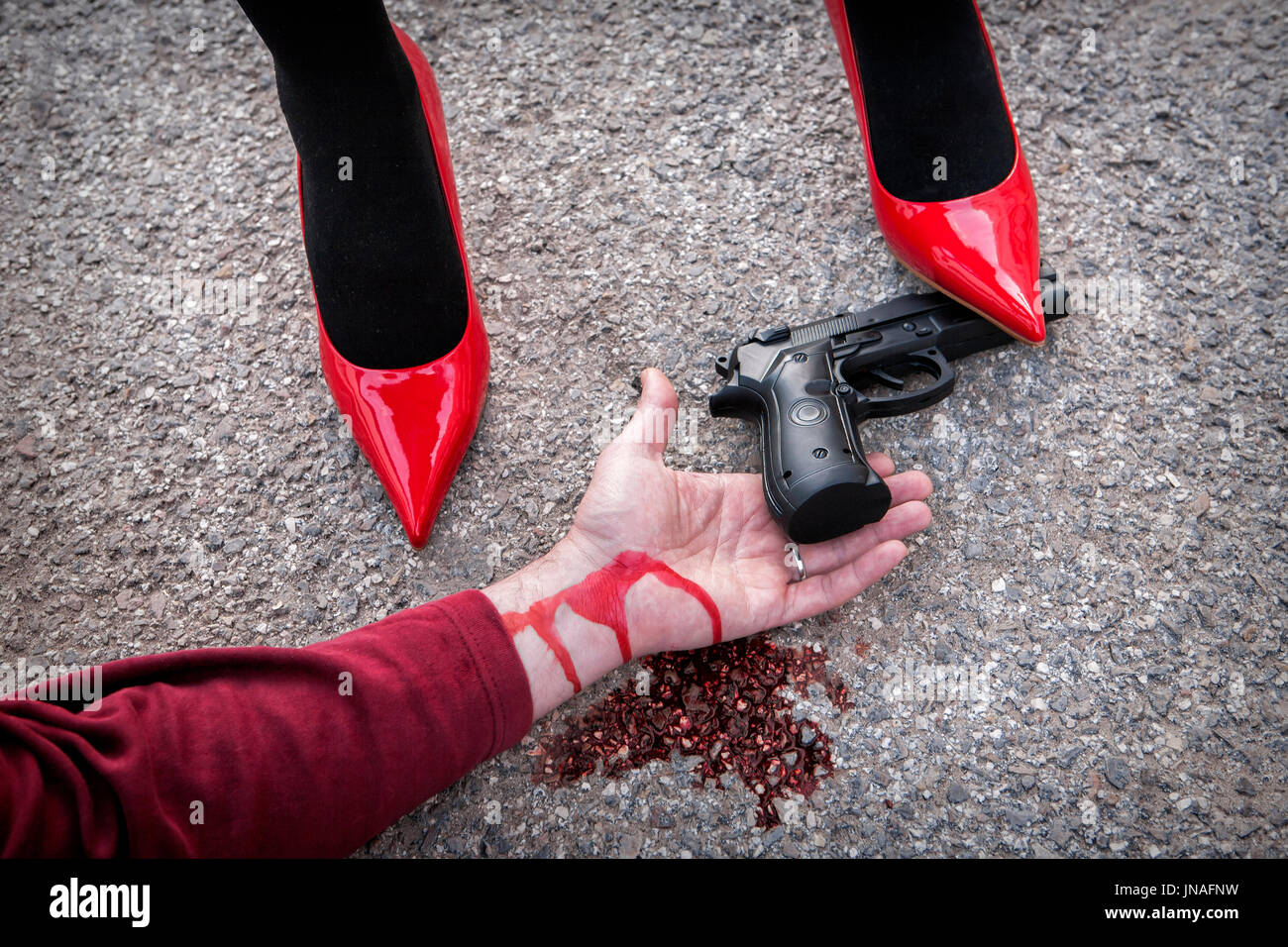 Man is dominated by a woman with red shoes, the shoe tread gun arm bloodied on the asphalt Stock Photo
