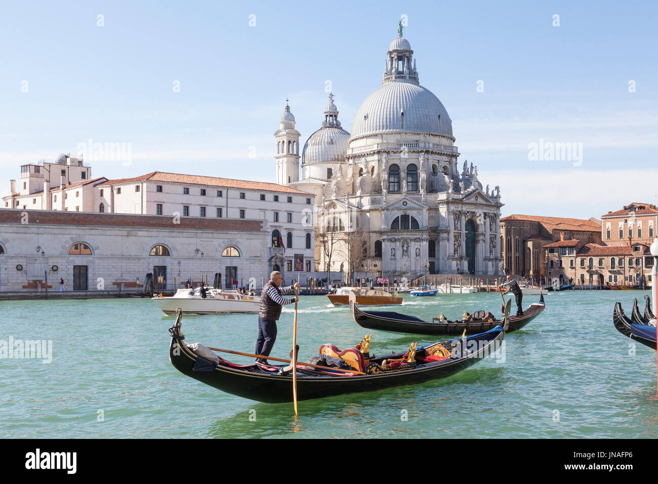 March 2017 Grand Canal, Venice, Italy. Two gondoliers rowing their gondolas past the Basilica Santa Maria della Salute with water taxis cruising by on Stock Photo