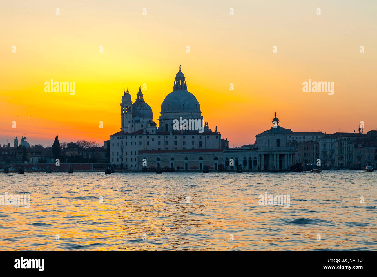Venice, Veneto, Italy. Dramatic orange sunset  over Basilica di Santa Maria della Salute and the Punta della Dogona, Dorsuduro, Venice  reflected in t Stock Photo