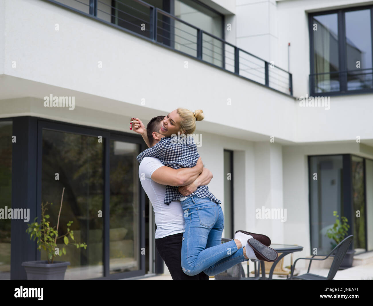 Portrait of a happy young couple hugging in front of their new luxury ...