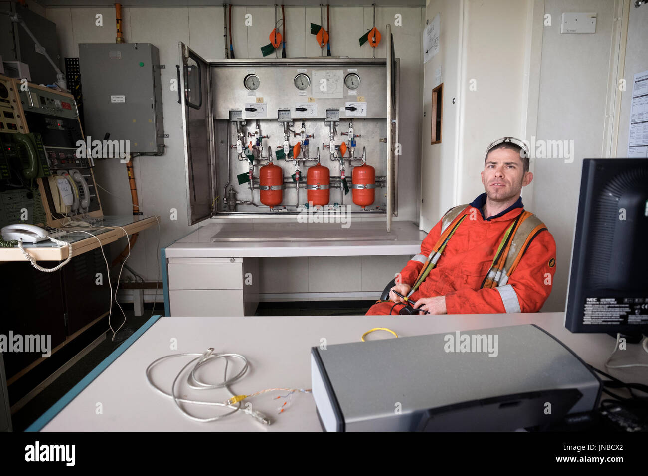 Oil and Gas worker, relaxed operator in a remote control room. Sat in red coveralls / overalls. credit: LEE RAMSDEN / ALAMY Stock Photo