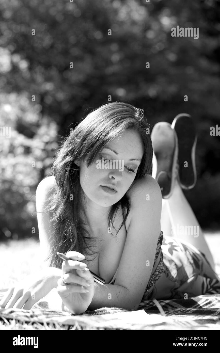 Beautiful red headed young woman lying on the grass in a low cut summer dress frock. Stock Photo