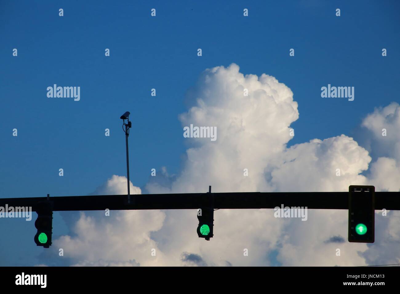 Three Green Traffic Lights with Camera on Post Above at Intersection
