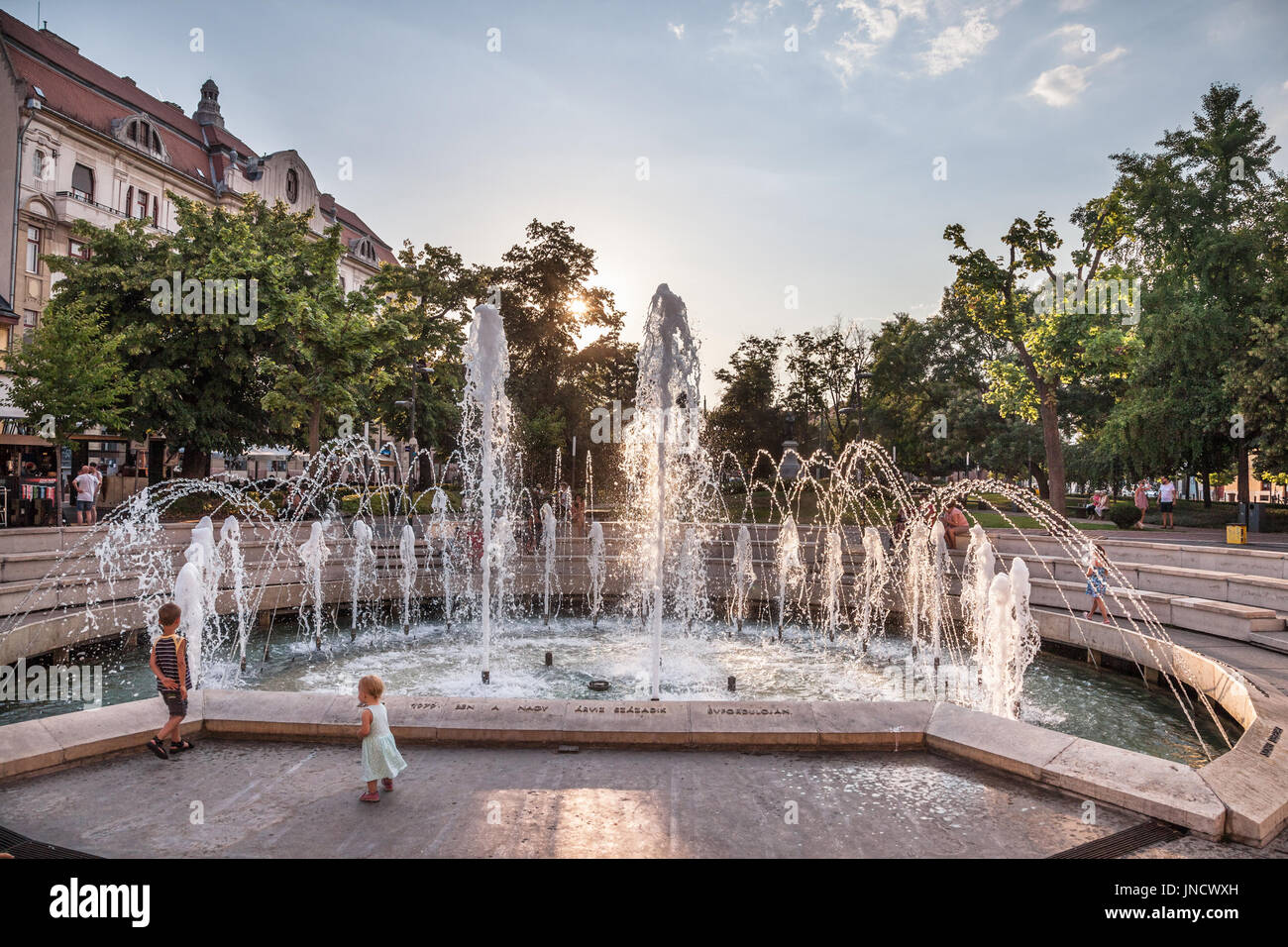 SZEGED, HUNGARY - JULY 20, 2017: Foutain on Dugonics Ter Square with children playing in front. This square, and the university building on it, are sy Stock Photo