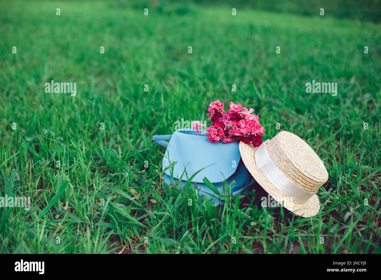Straw hat and romantic wild-flower bunch bouquet on green grass lawn. Stock Photo