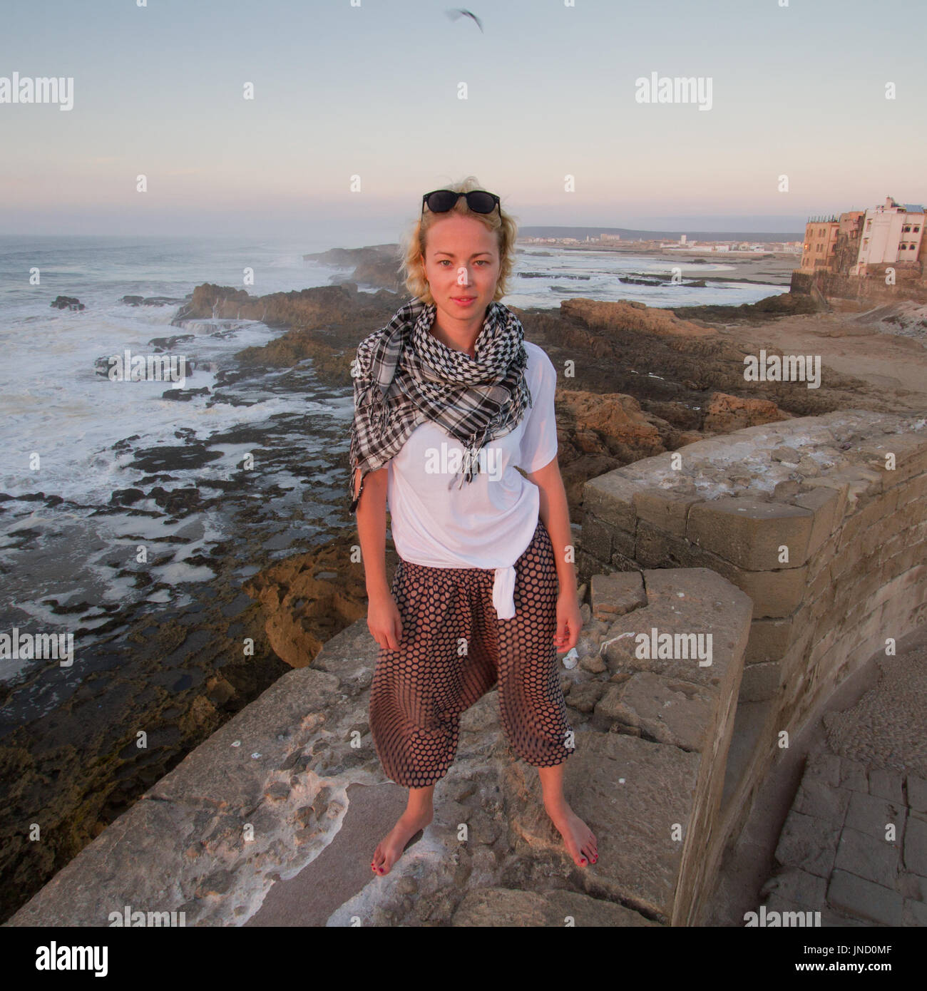Female traveler standing barefooted on city fortress wall of Essaouira, Morocco. Stock Photo