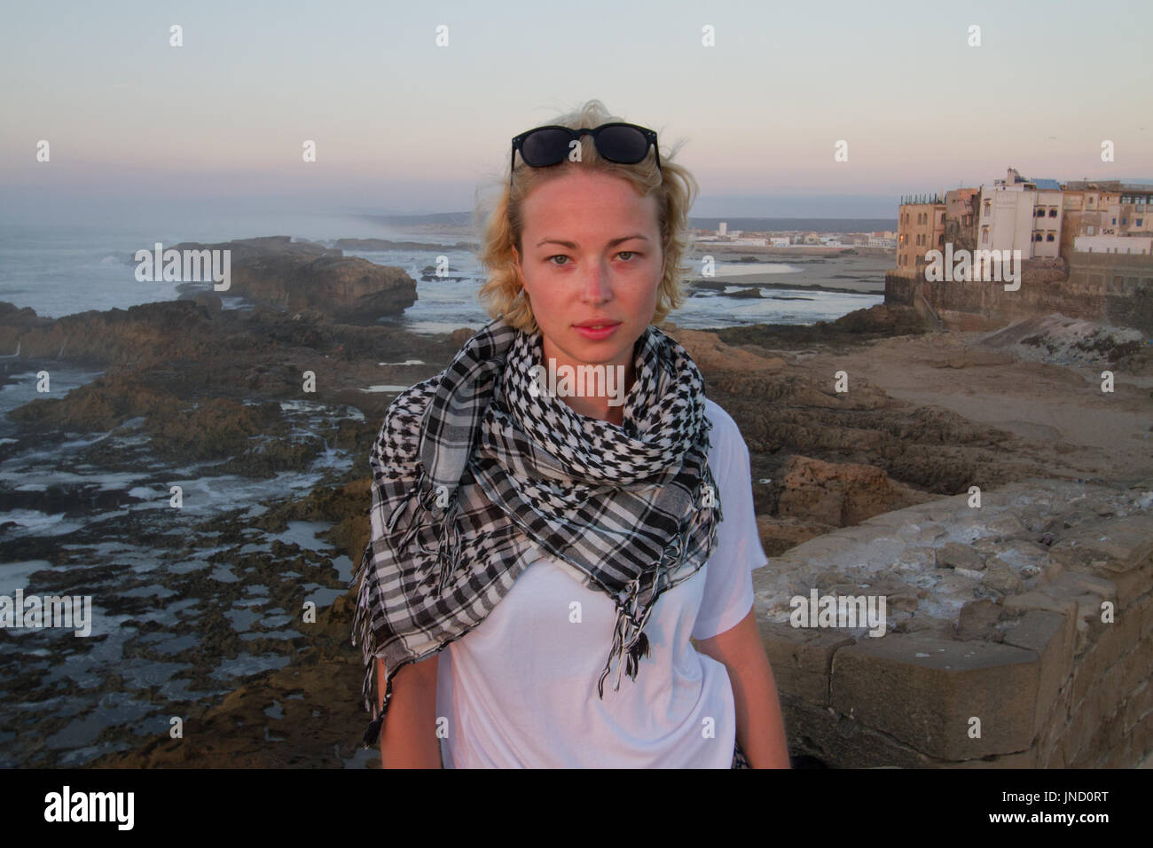 Female traveler standing on city fortress wall of Essaouira, Morocco in sunset. Stock Photo