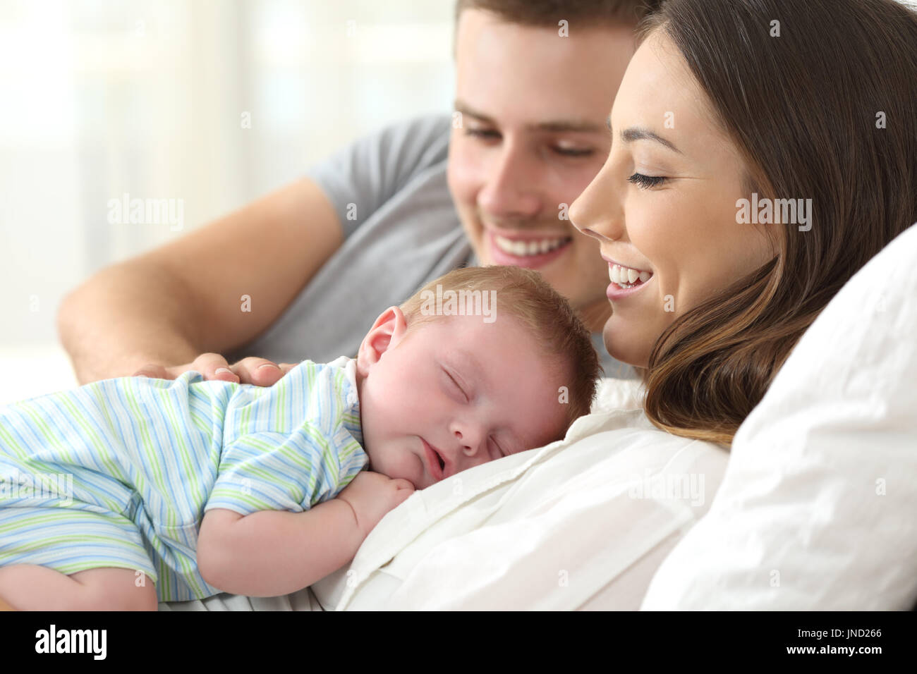 Happy parents watching their baby sleeping on a bed at home Stock Photo