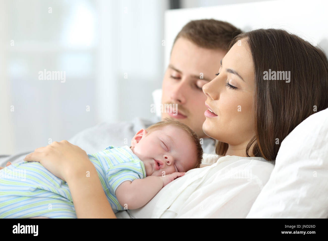 Portrait of tired parents sleeping with their baby on a bed at home Stock Photo