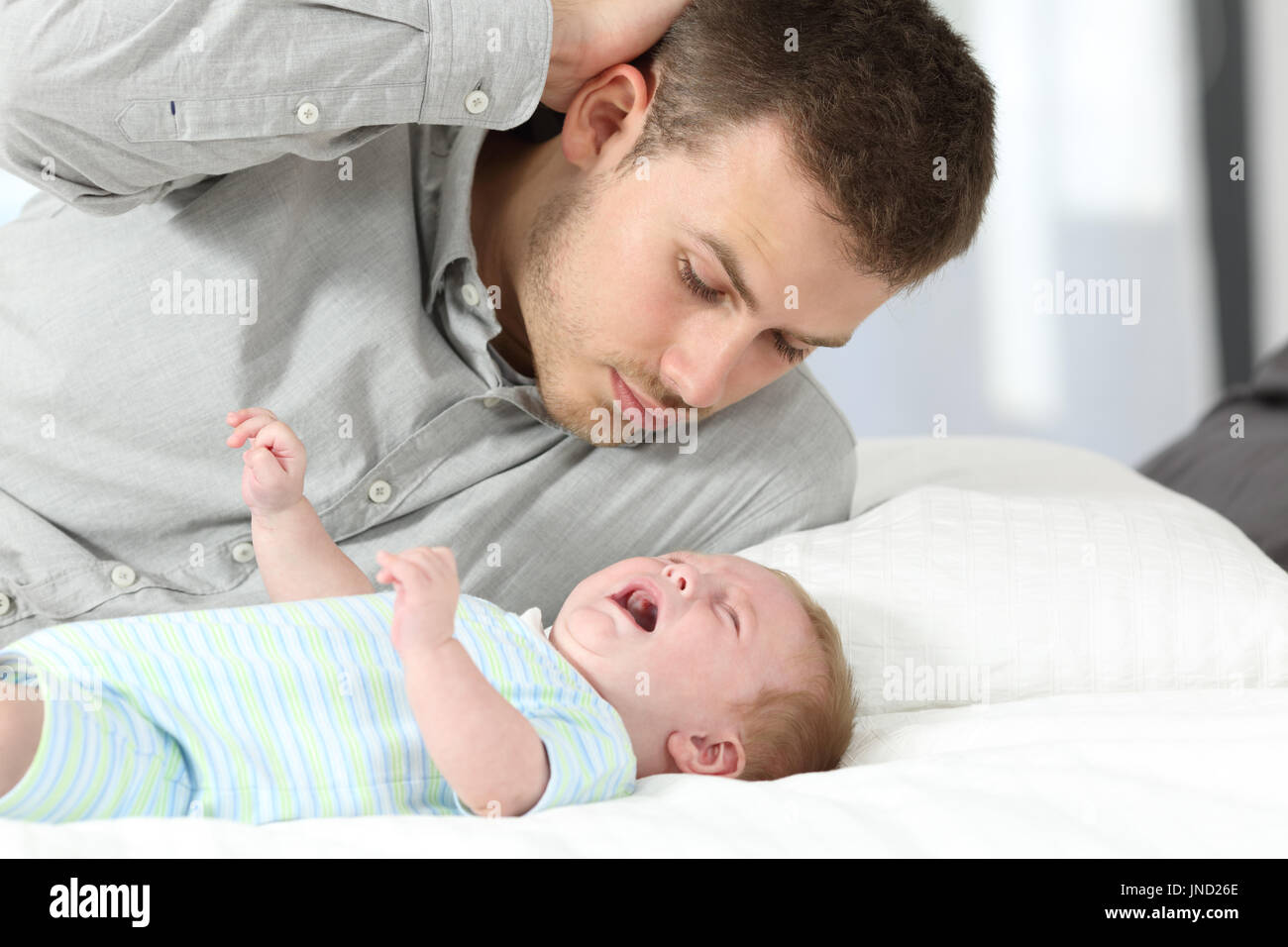 Confused father watching his baby son crying desperately on a bed Stock Photo