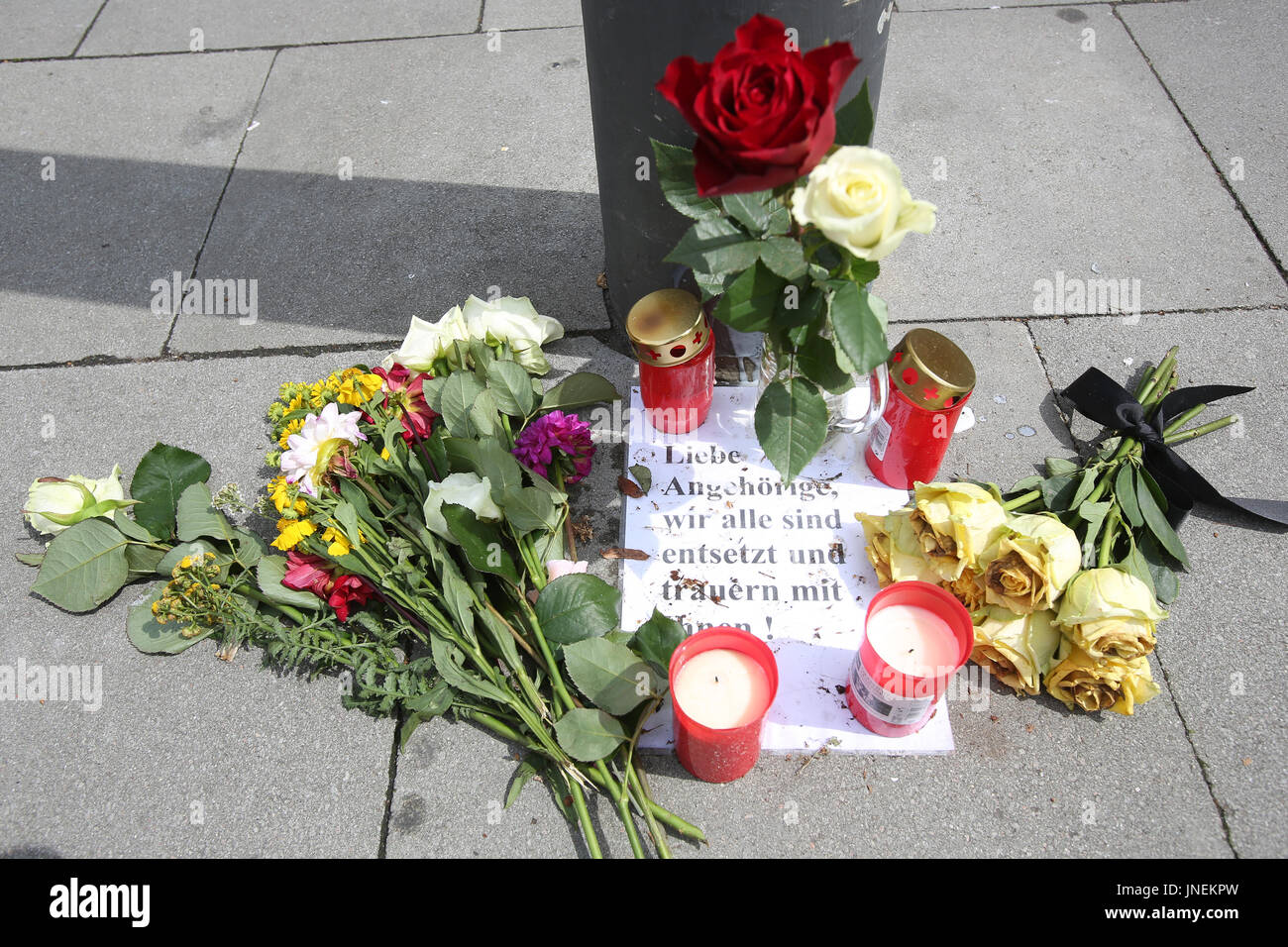 Hamburg, Germany. 30th July, 2017. A note reading 'Liebe Angehoerige, wir sind alle entsetzt und trauern mit euch' (lit. 'Dear family members, we are all shocked and mourn with you') can be seen between candles and flowers at a bus stop near a supermarket in which a man had killed another person an injured six further people with a knife in the district of Barmbek in Hamburg, Germany, 30 July 2017. Photo: Bodo Marks/dpa/Alamy Live News Stock Photo