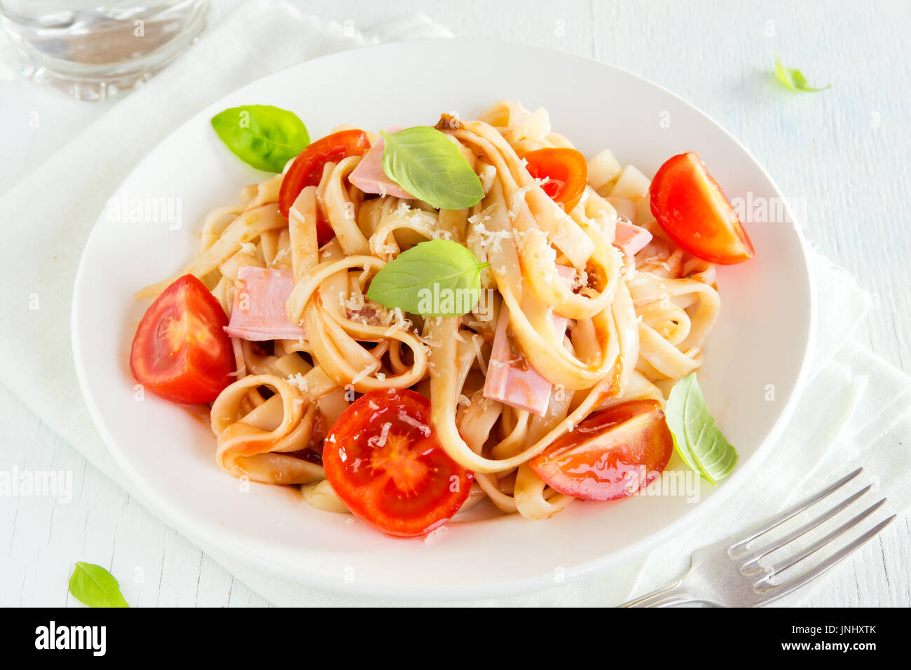 Tagliatelle pasta with ham, tomato sauce, cherry tomatoes and basil
