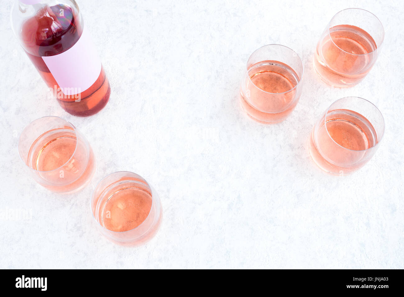 Rose Wine bottle and glasses filled with wine on white marbled background. Stock Photo
