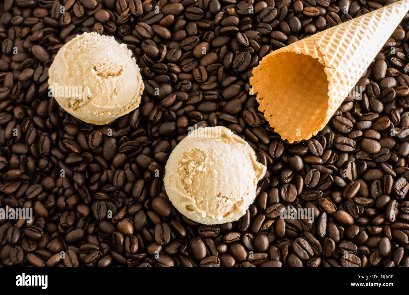 Two scoops of homemade coffee ice cream and an empty ice cream cone on whole dark roasted coffee beans. Stock Photo
