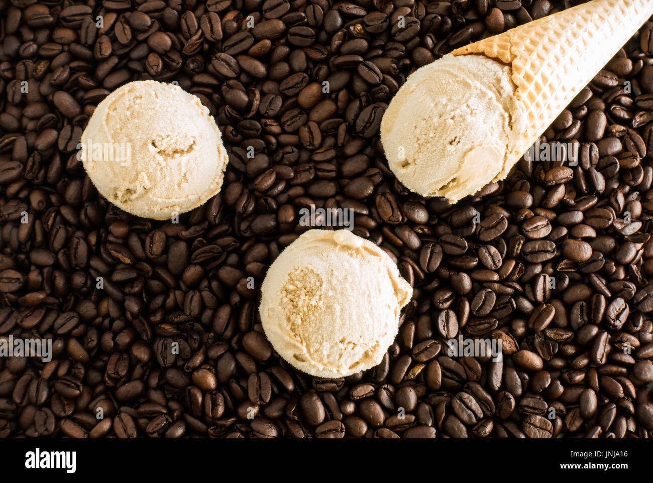 Scoops of homemade coffee ice cream and ice cream cone on whole dark roasted coffee beans Stock