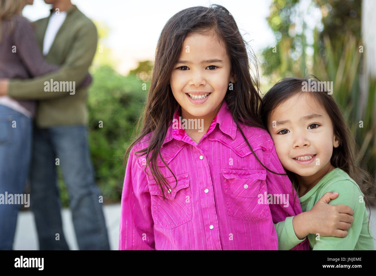 Happy little girls with their parents in the background. Stock Photo