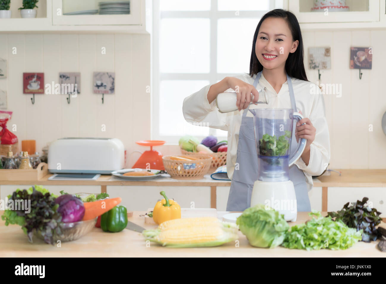 Vegetable smoothie. Asian woman making green smoothies with blender home in kitchen. Healthy raw eating lifestyle concept portrait of beautiful young  Stock Photo