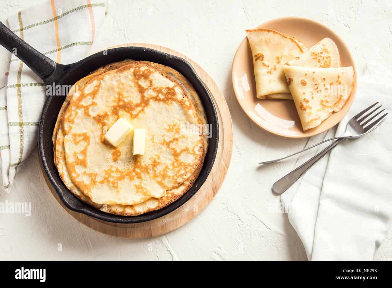 Homemade crepes with butter in cast iron pan over white background