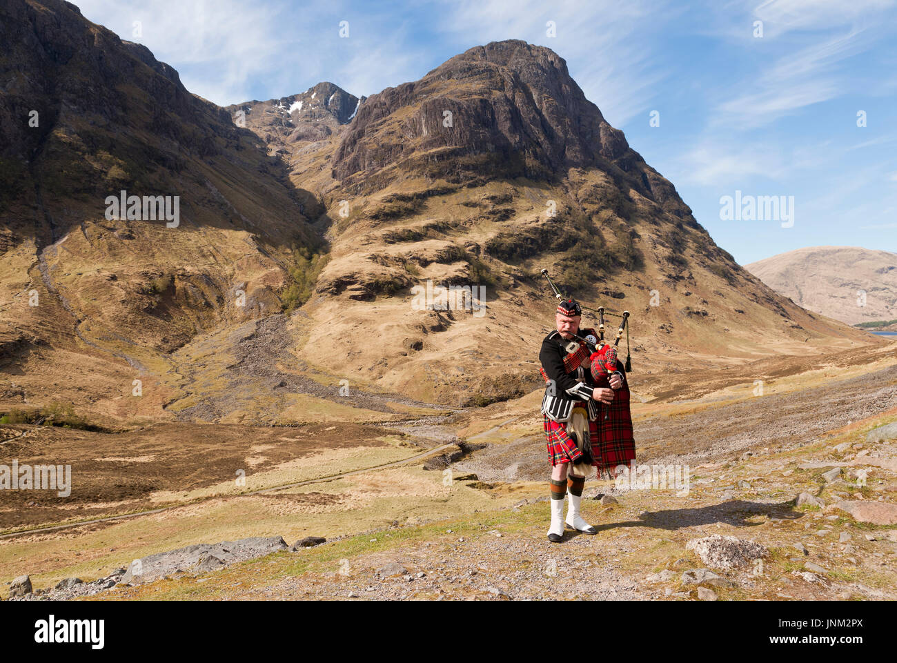A piper playing the bagpipes with a Scottish mountain backdrop Stock Photo