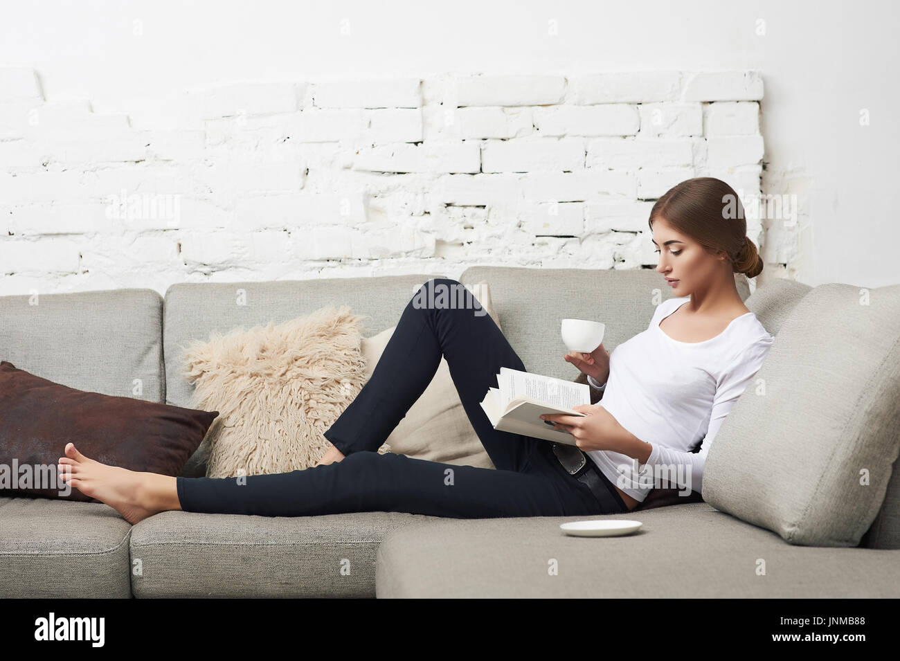 Young beautiful woman sitting on the sofa reading a book holding her