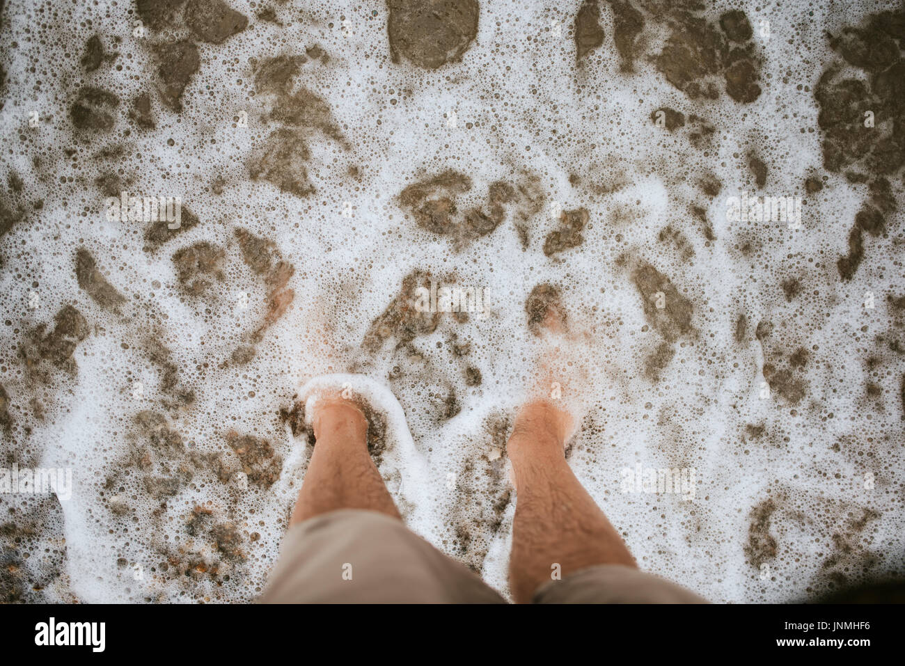 Bare feet on the beach covered with sea foam Stock Photo