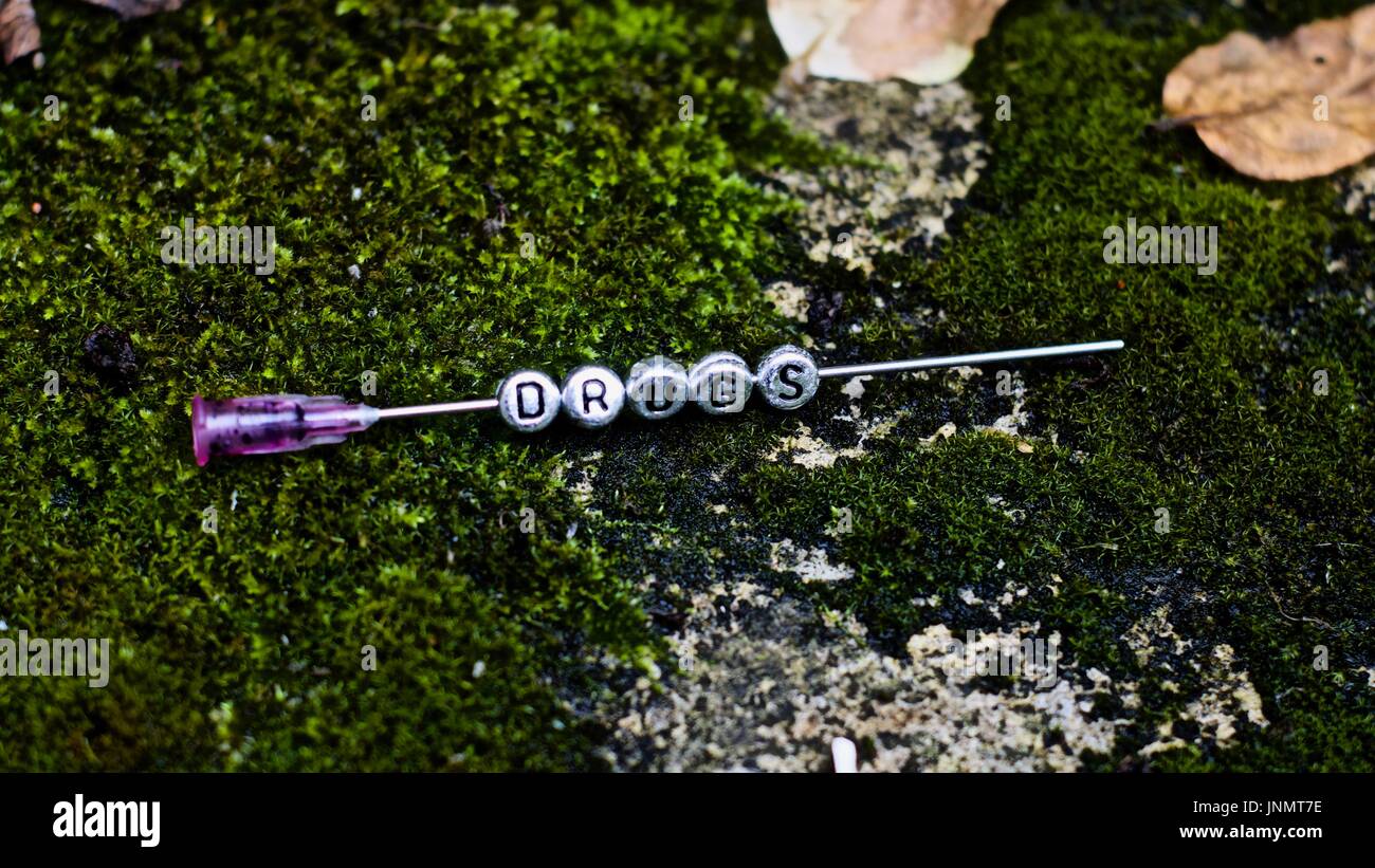 Silver inscription on the needle in green grass. Drugs on the needle. Stock Photo