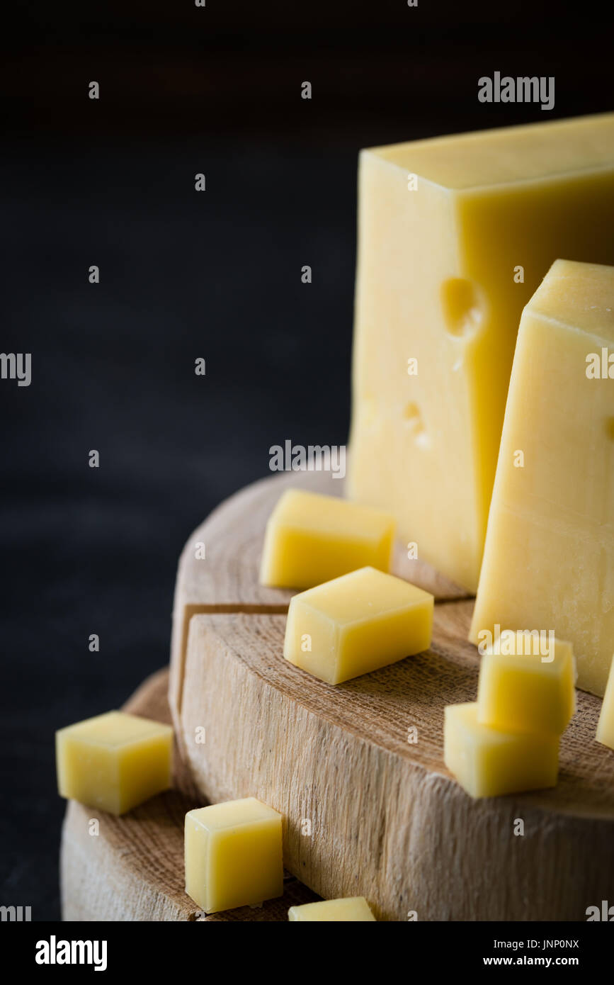 Closeup of Swedish hard yellow cheese with holes chopped on wooden slices on dark rustic background Stock Photo