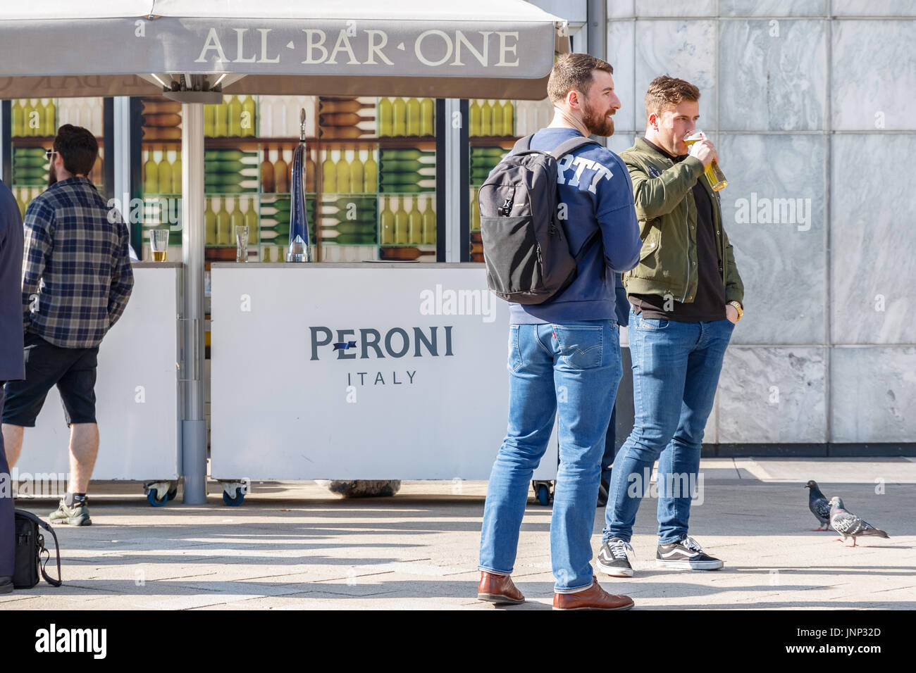 London, UK - May 10, 2017 - Two men drinking beer outside a bar in Canary Wharf on a sunny day Stock Photo