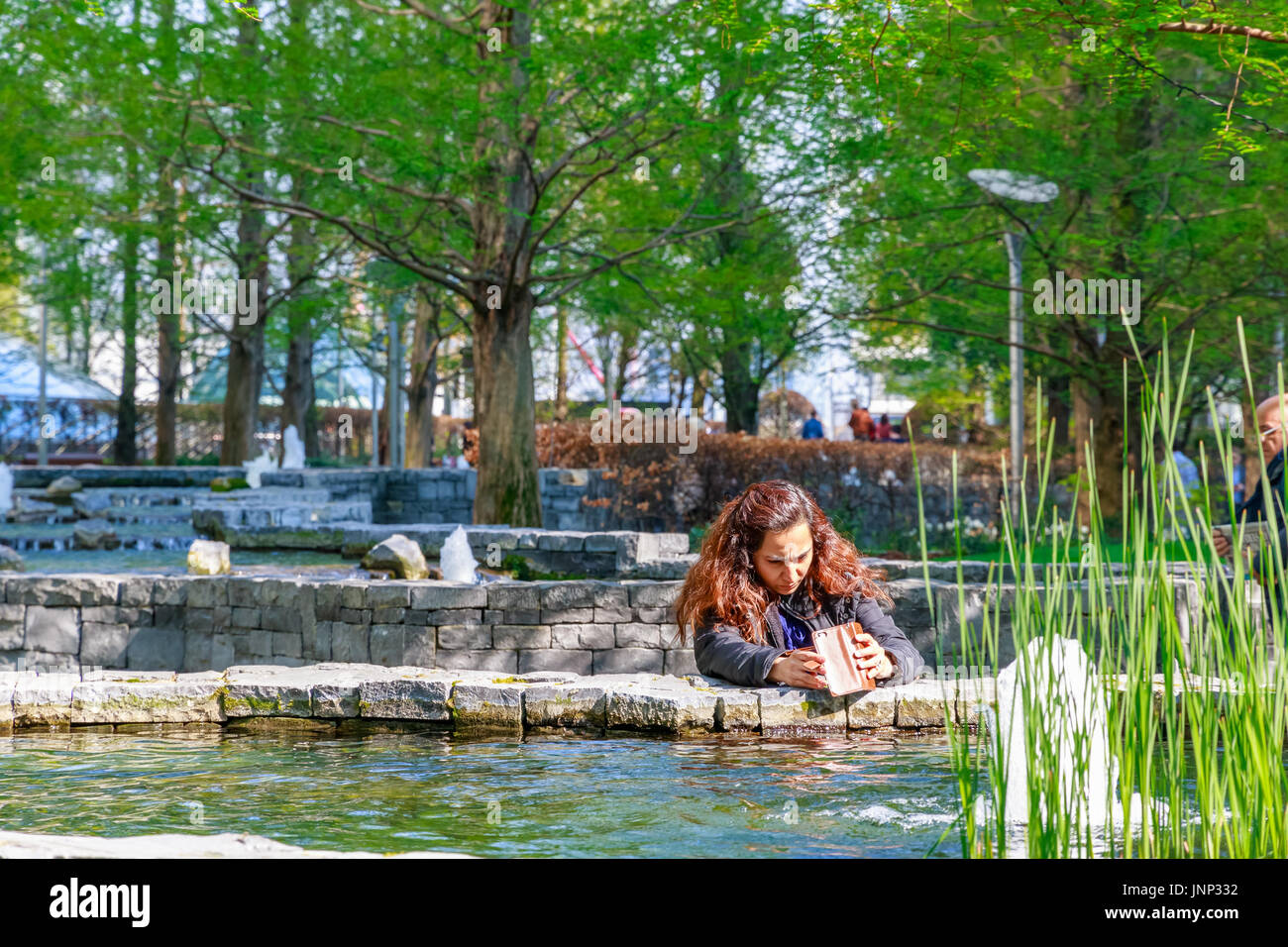 London, UK - May 10, 2017 - A woman taking pictures in Jubilee Park, a landscaped space in Canary Wharf Stock Photo
